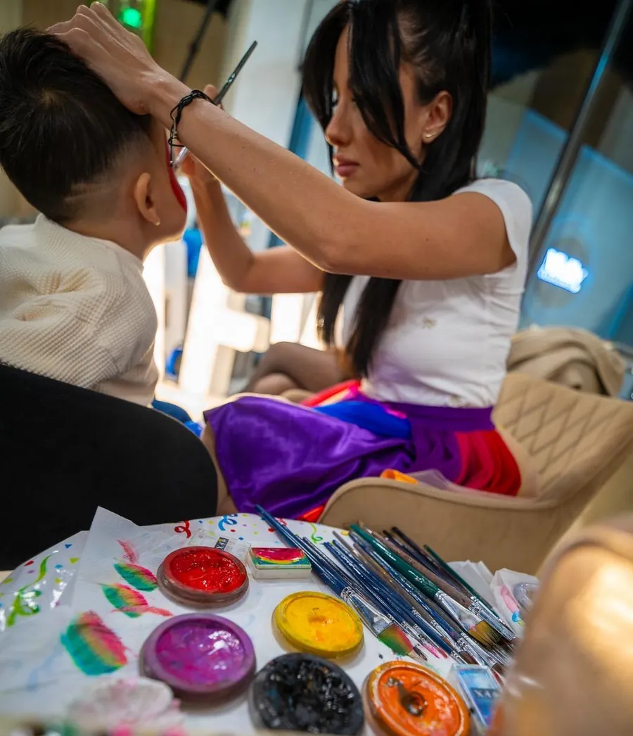 Anca Marinică pictând fața unui copil, cu vopselele de face painting pe masă