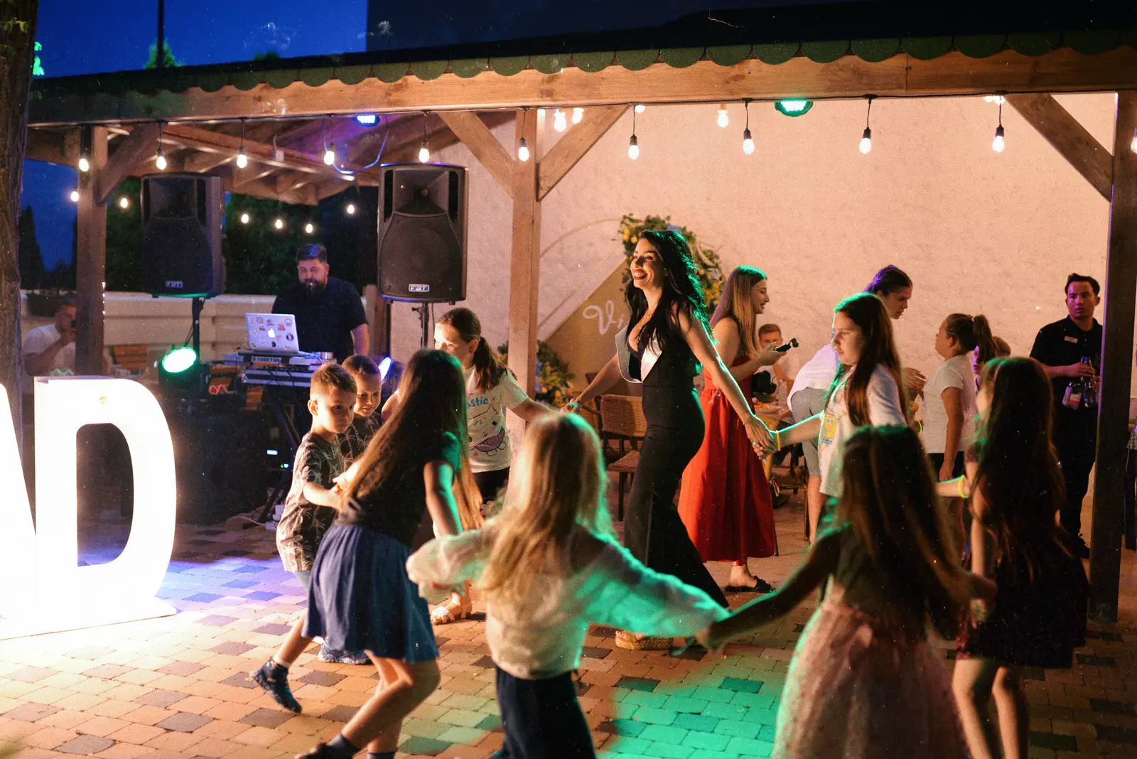 Petrecere în aer liber seara, cu copii care dansează lângă DJ