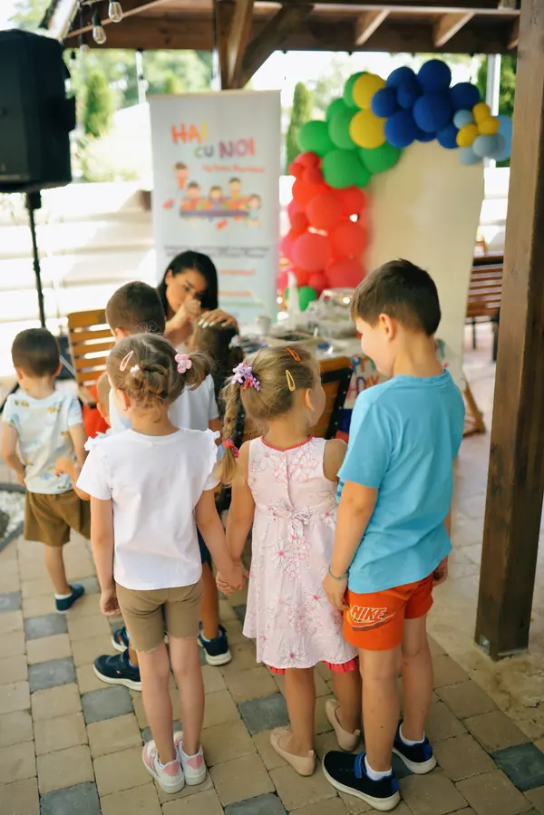 Copii la masa de activități, în fața bannerului Hai cu noi la joacă